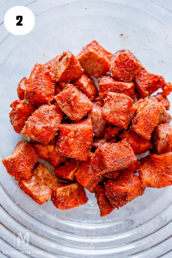 Cubed pieces of raw salmon coated with red seasoning in a clear glass mixing bowl, viewed from above.