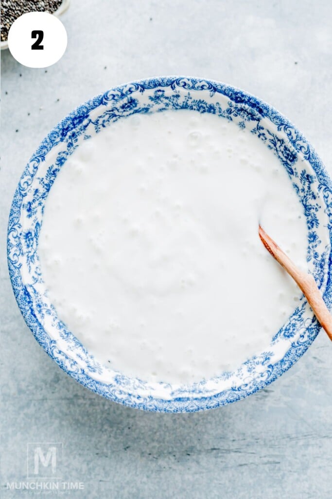 A blue and white patterned bowl filled with a smooth white mixture, with a wooden spoon resting inside, placed on a light surface.