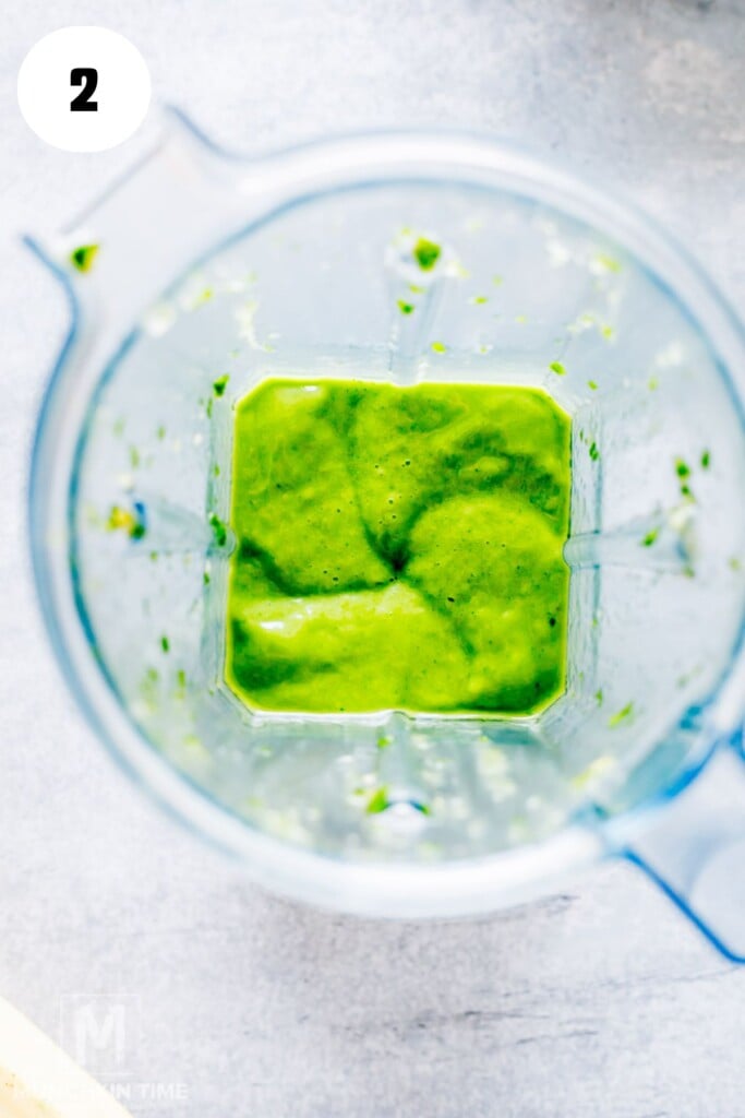 A top-down view of a blender containing a thick, bright green sauce or smoothie mixture.