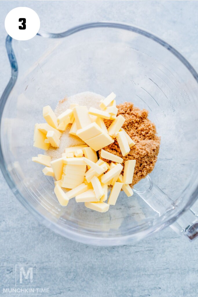 Chopped butter, granulated sugar, and brown sugar in a clear mixing bowl, viewed from above. Step 3 is indicated in the corner.