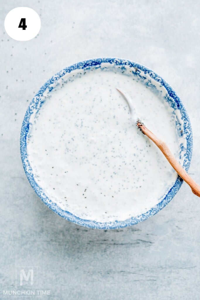 Blue-patterned bowl filled with creamy white sauce speckled with herbs; a small wooden-handled spoon rests inside the bowl on a light surface.