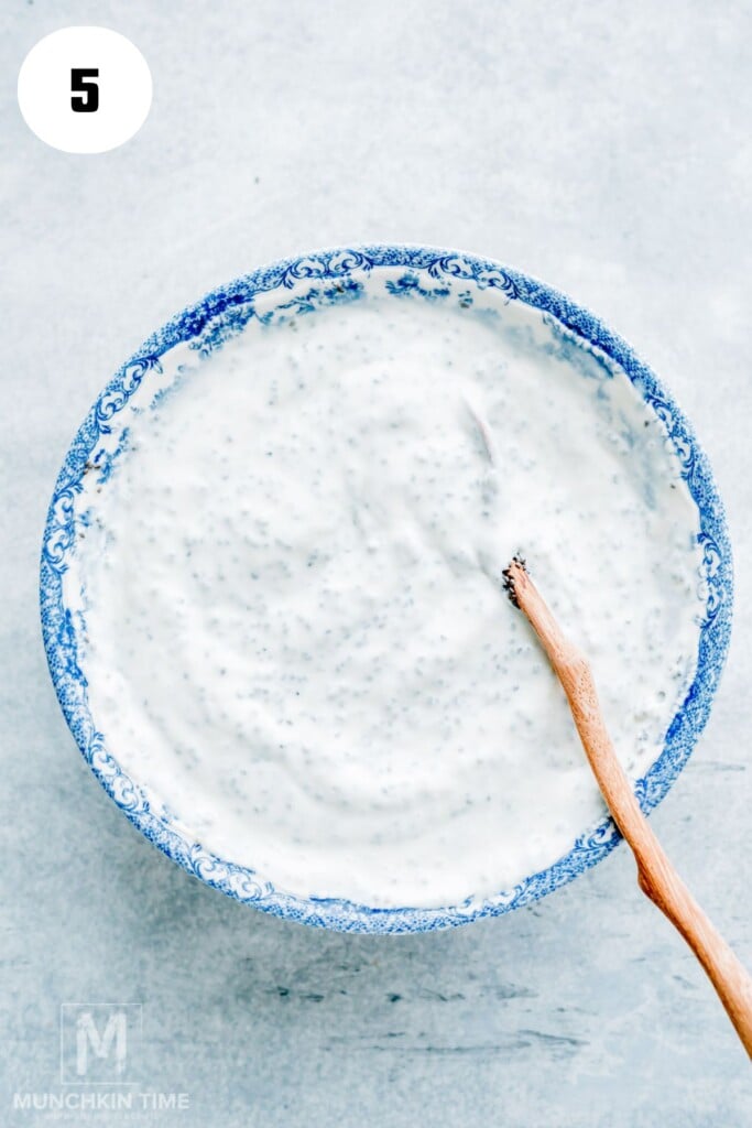 A blue and white bowl filled with chia pudding mixture, with a wooden spoon resting inside, viewed from above on a light surface.