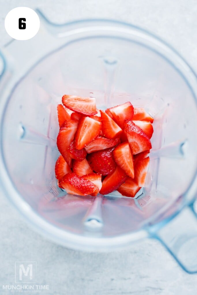 Sliced strawberries in a blender viewed from above, ready for blending.