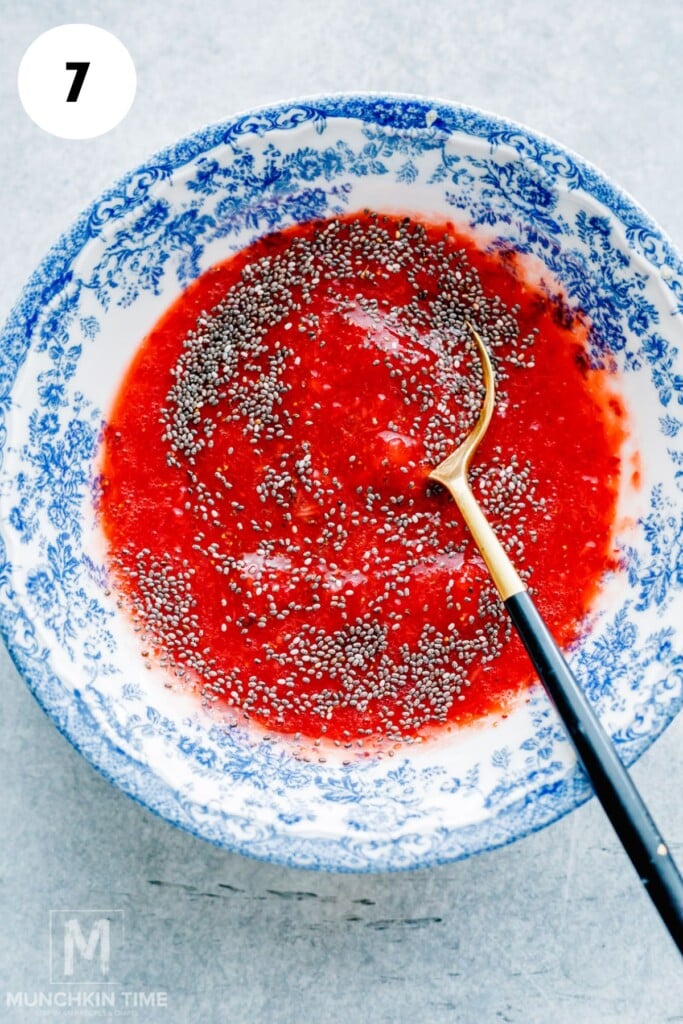A blue and white bowl containing a red mixture with chia seeds, with a black and gold spoon resting inside.