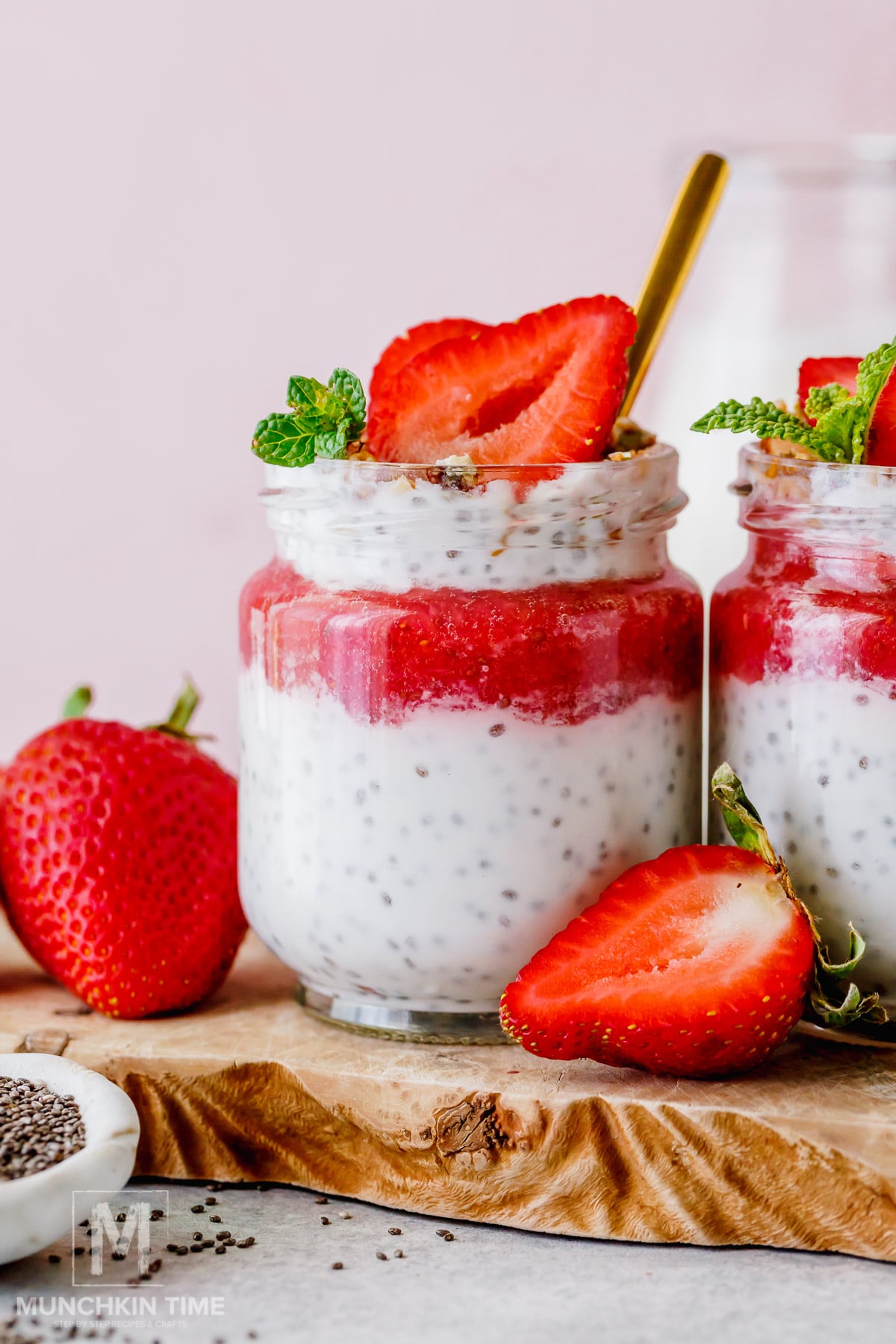 A jar of chia pudding topped with strawberry puree, a sliced strawberry, and mint leaves, placed on a wooden board with fresh strawberries nearby.