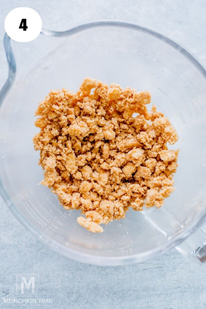 A glass mixing bowl containing a crumbly brown sugar mixture, viewed from above. Step 4 indicator in the top left corner.