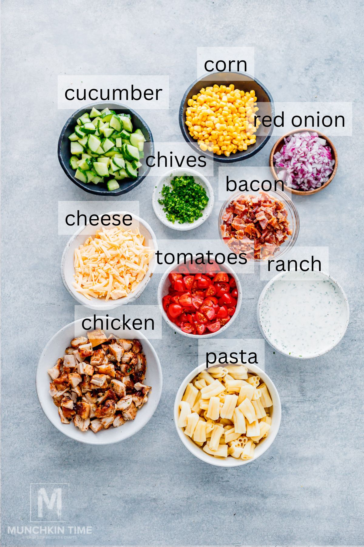 Ingredients for Chicken Pasta Salad, including pasta, chicken, bacon, corn, cucumber, tomatoes, red onion, cheddar cheese, chives, and homemade ranch dressing.