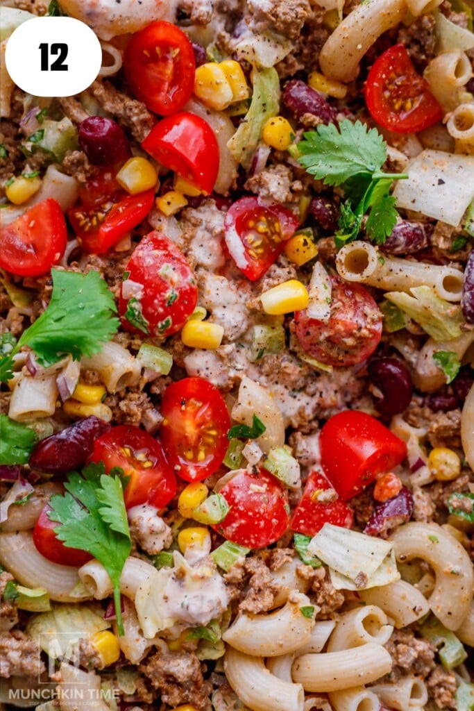 Close-up of a pasta salad with ground meat, cherry tomatoes, red kidney beans, corn, lettuce, chopped cilantro, and a creamy dressing.