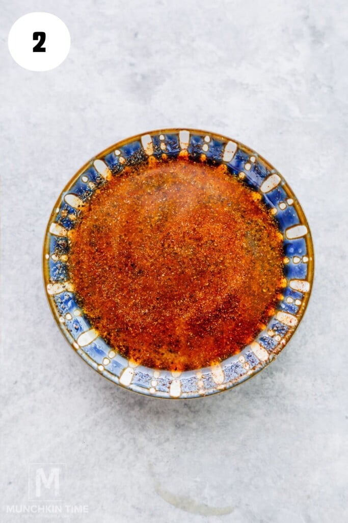 A round bowl with an orange-red spice mixture sits on a light gray surface. The bowl has a blue and white patterned rim.