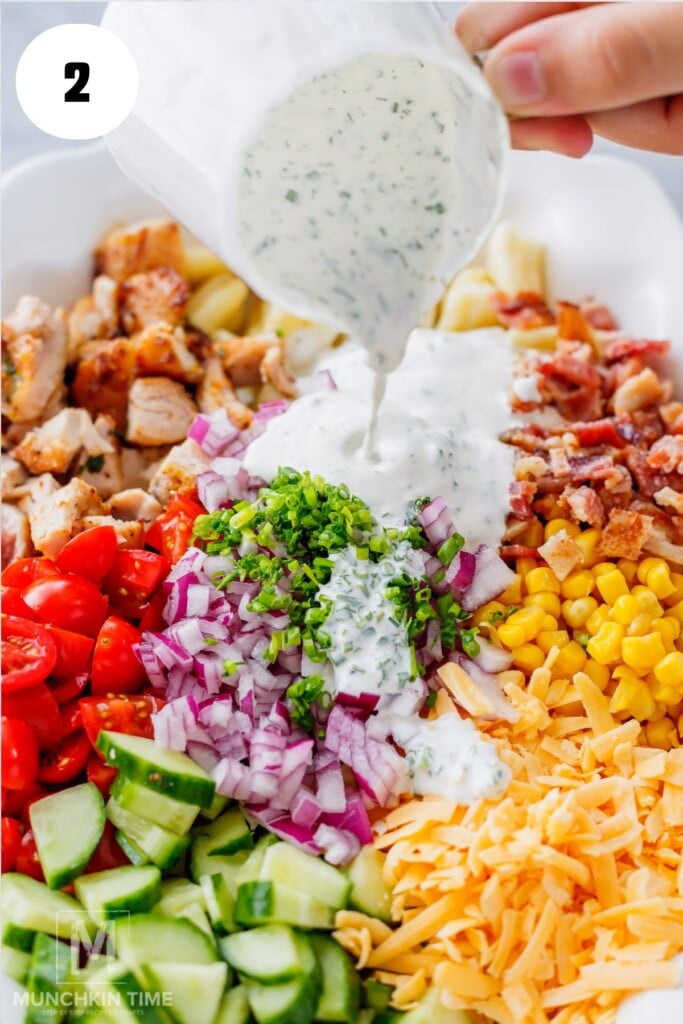 Pouring creamy homemade ranch dressing over Chicken Bacon Ranch Pasta Salad ingredients.