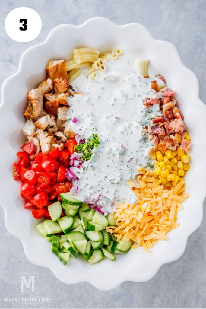 Adding cooked pasta, chicken, bacon, vegetables, cheese, dressing and chives to a large mixing bowl.