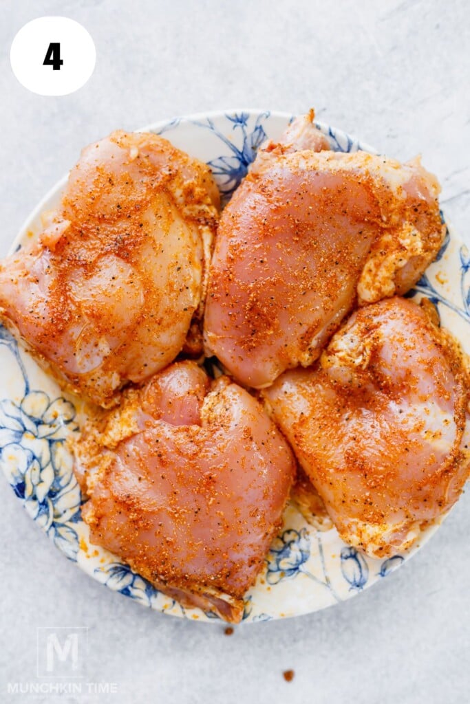 Four raw, seasoned chicken thighs on a floral-patterned plate, viewed from above.