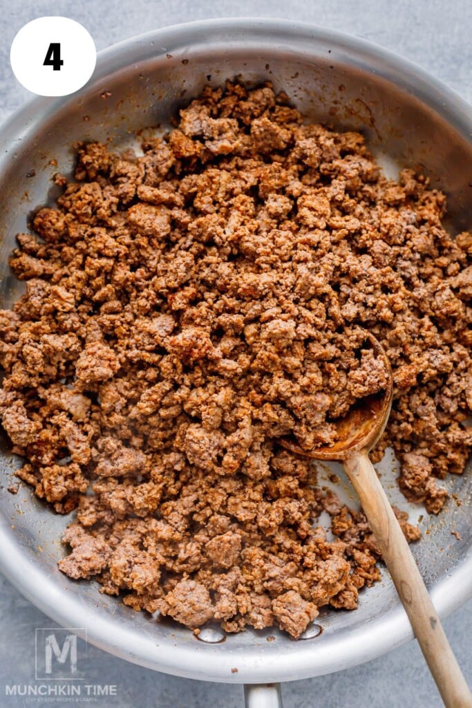 Cooked ground beef in a sauté pan with a wooden spoon, shown from above.