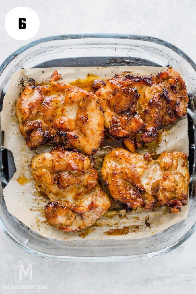 Four cooked, seasoned air fryer chicken thighs in a glass baking dish lined with parchment paper, viewed from above.