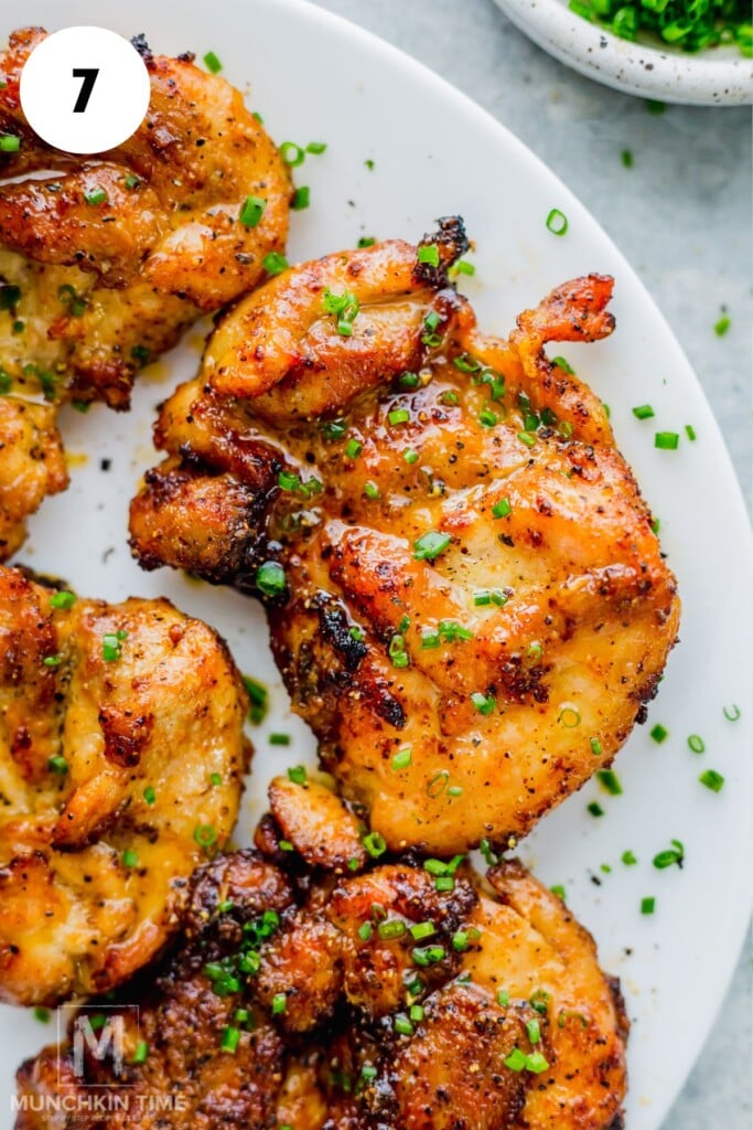 Seasoned air fryer chicken thighs garnished with chopped chives, served on a white plate.