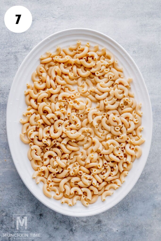 An oval white plate filled with cooked elbow macaroni pasta is placed on a light gray surface.