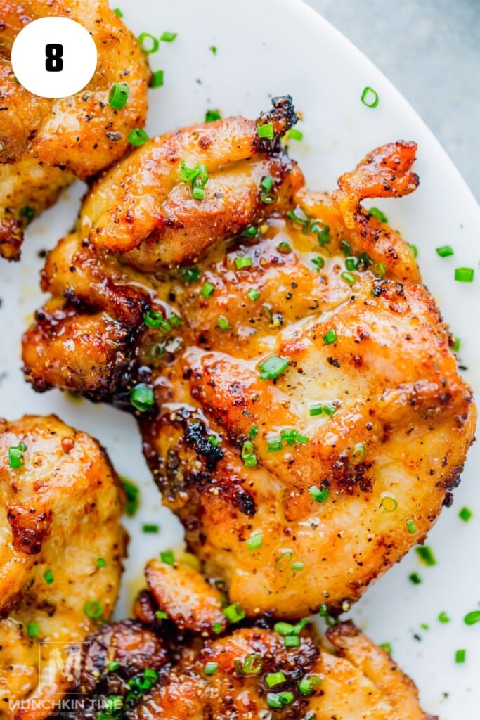 Close-up of grilled air fryer chicken thighs garnished with chopped chives, served on a white plate.