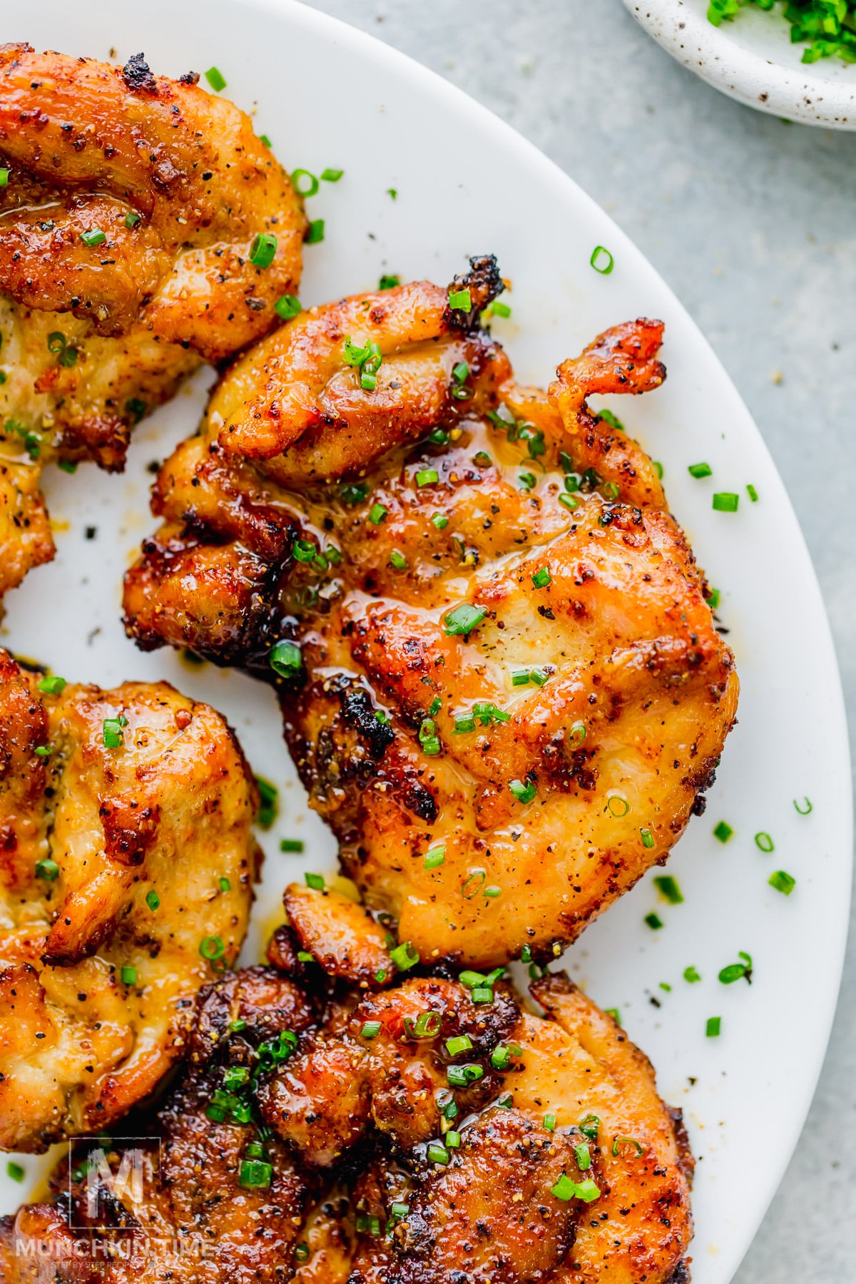 Air fryer chicken thighs garnished with chopped chives on a white plate.