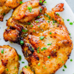 Close-up of seasoned, air fryer chicken thighs garnished with chopped chives, served on a white plate.
