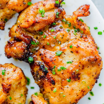 Close-up of seasoned, air fryer chicken thighs garnished with chopped chives, served on a white plate.
