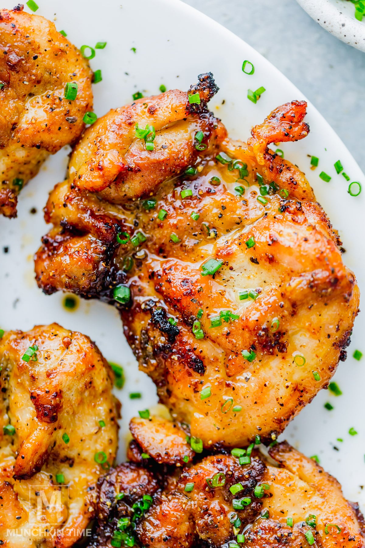 Close-up of roasted, seasoned air fryer chicken thighs garnished with chopped chives on a white plate.