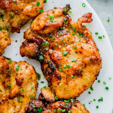 Grilled, seasoned air fryer chicken thighs garnished with chopped chives, served on a white plate.