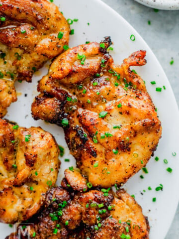 Grilled, seasoned air fryer chicken thighs garnished with chopped chives, served on a white plate.