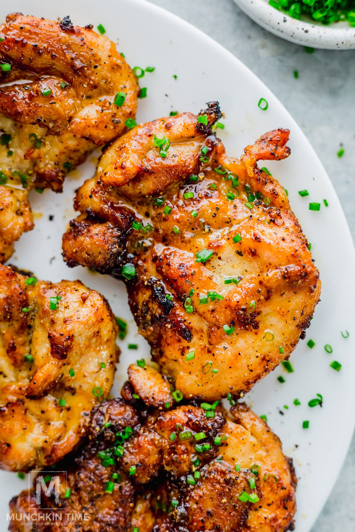 Grilled, seasoned air fryer chicken thighs garnished with chopped chives, served on a white plate.