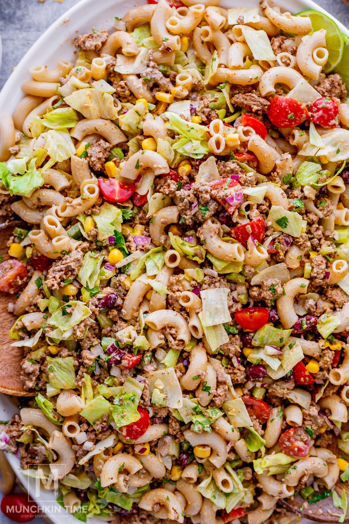 A plate of taco pasta salad with macaroni, ground meat, chopped lettuce, cherry tomatoes, corn, and red onion.