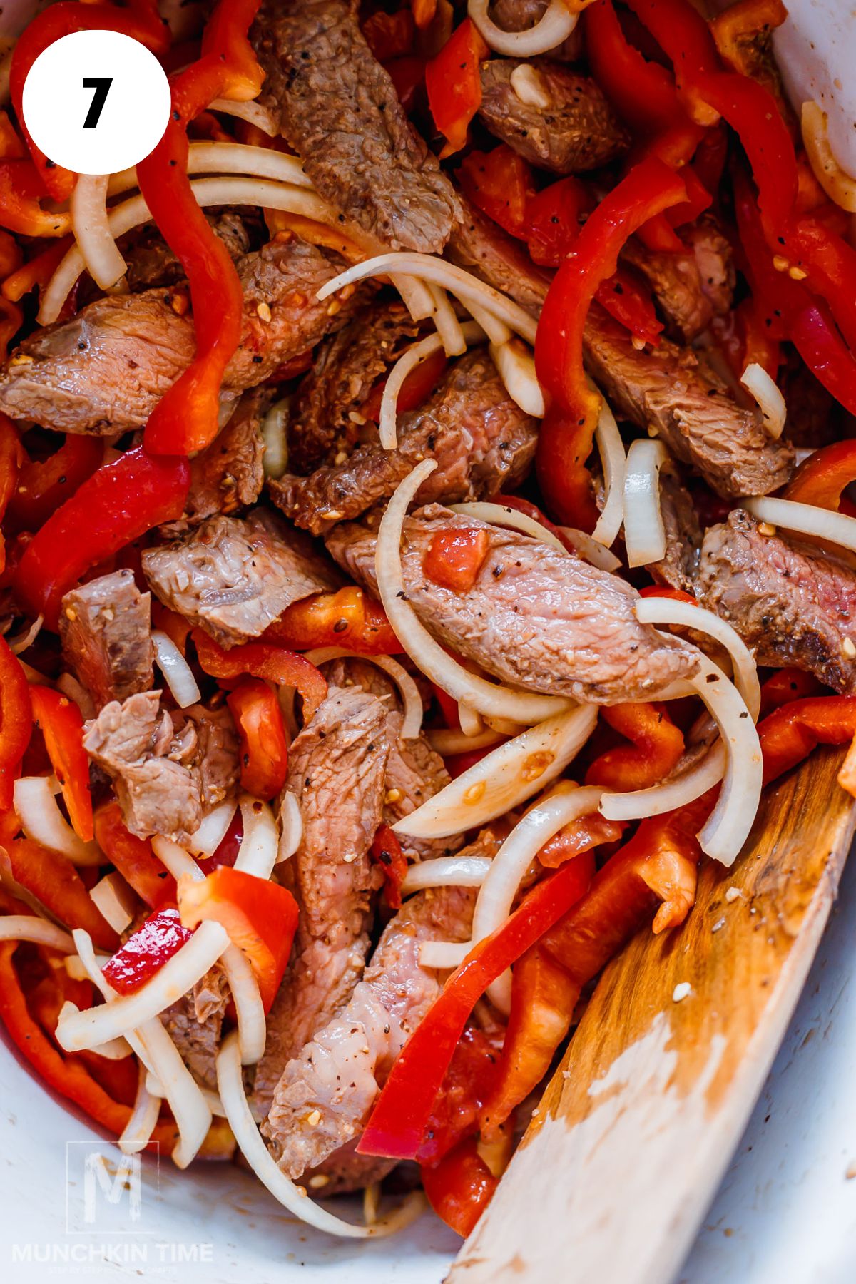 beef, bell peppers and onions mixed in a crock pot bowl.