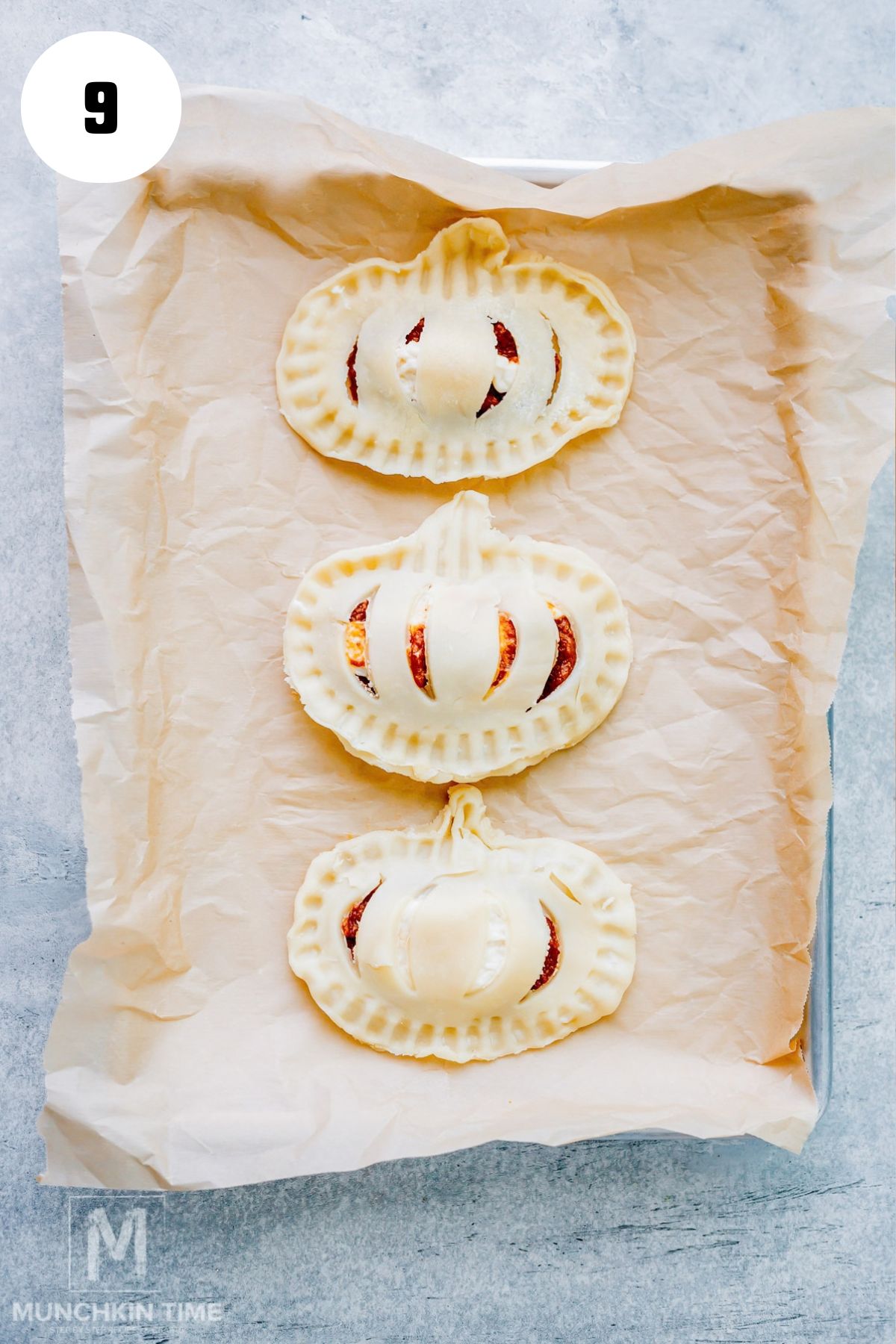 Unbaked pumpkin cream cheese hand pies arranged on a parchment-lined baking sheet.
