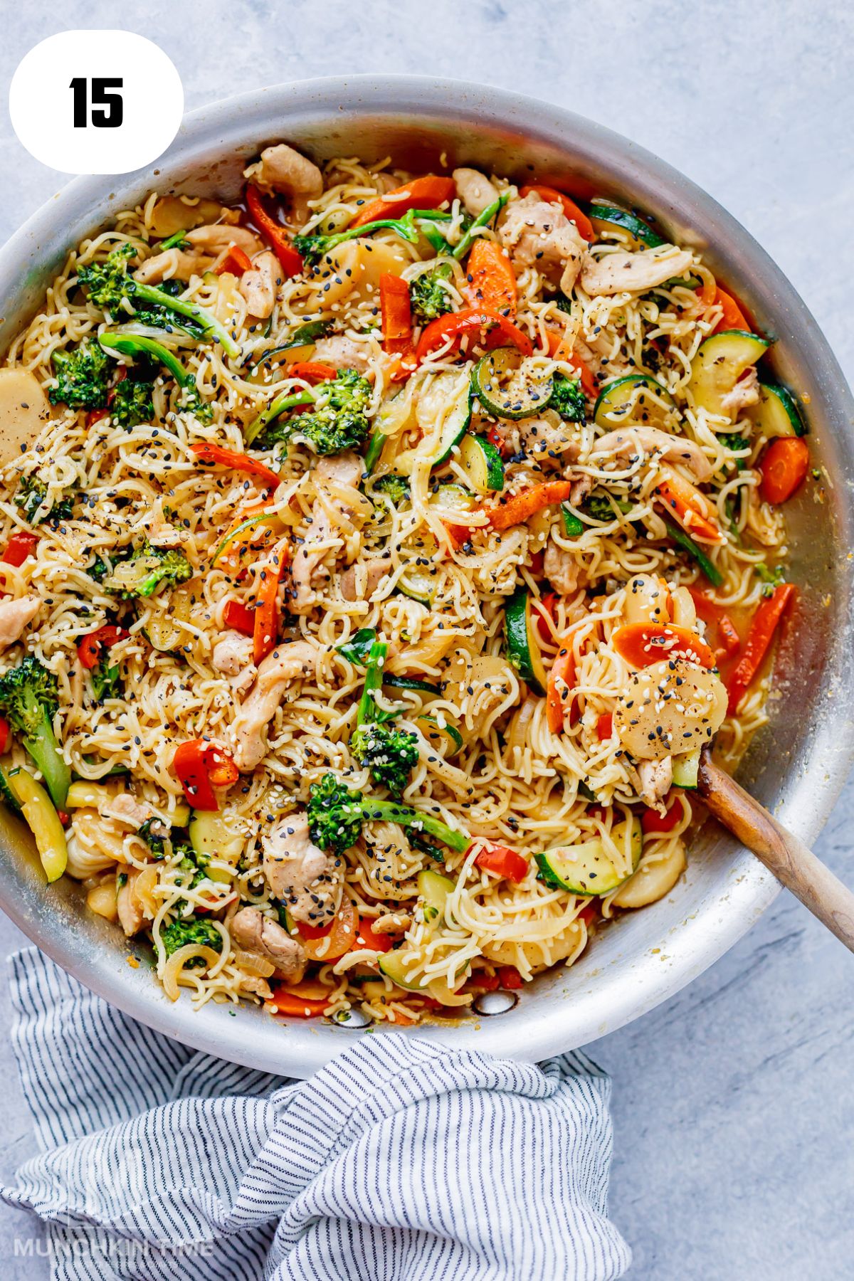 Tossing noodles, chicken and vegetables with lo mein sauce in a skillet.