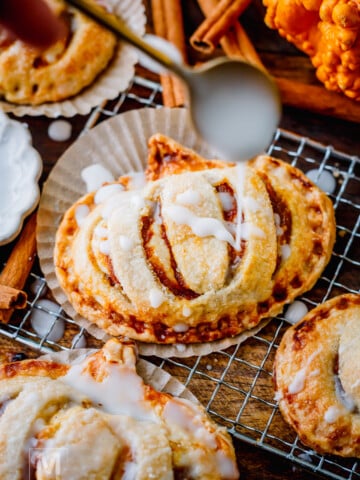 Golden pumpkin hand pies stacked and drizzled with simple glaze for a cozy fall dessert.