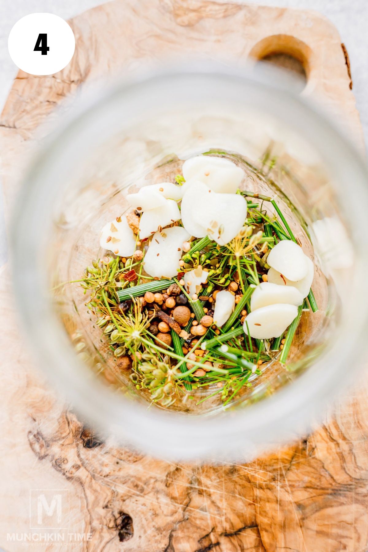 Fresh garlic, dill florets and stalks added to the bottom of a glass jar