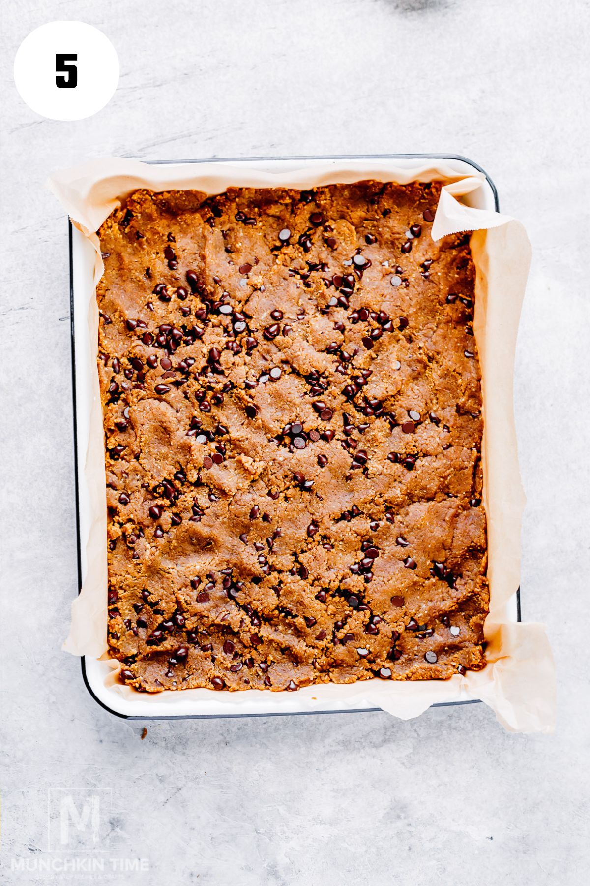 Pressing chocolate chip cookie dough into a parchment-lined square baking pan