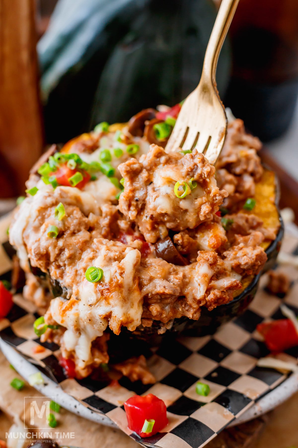 Close-up of cheesy ground beef stuffed acorn squash with melted cheddar and mozzarella, refried beans, fresh tomatoes, avocado, and cilantro.