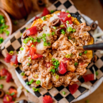 Stuffed acorn squash with ground beef topped with cheese, diced tomatoes, and fresh cilantro