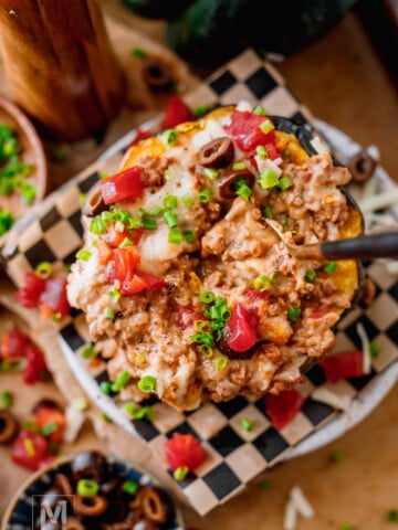 Stuffed acorn squash with ground beef topped with cheese, diced tomatoes, and fresh cilantro