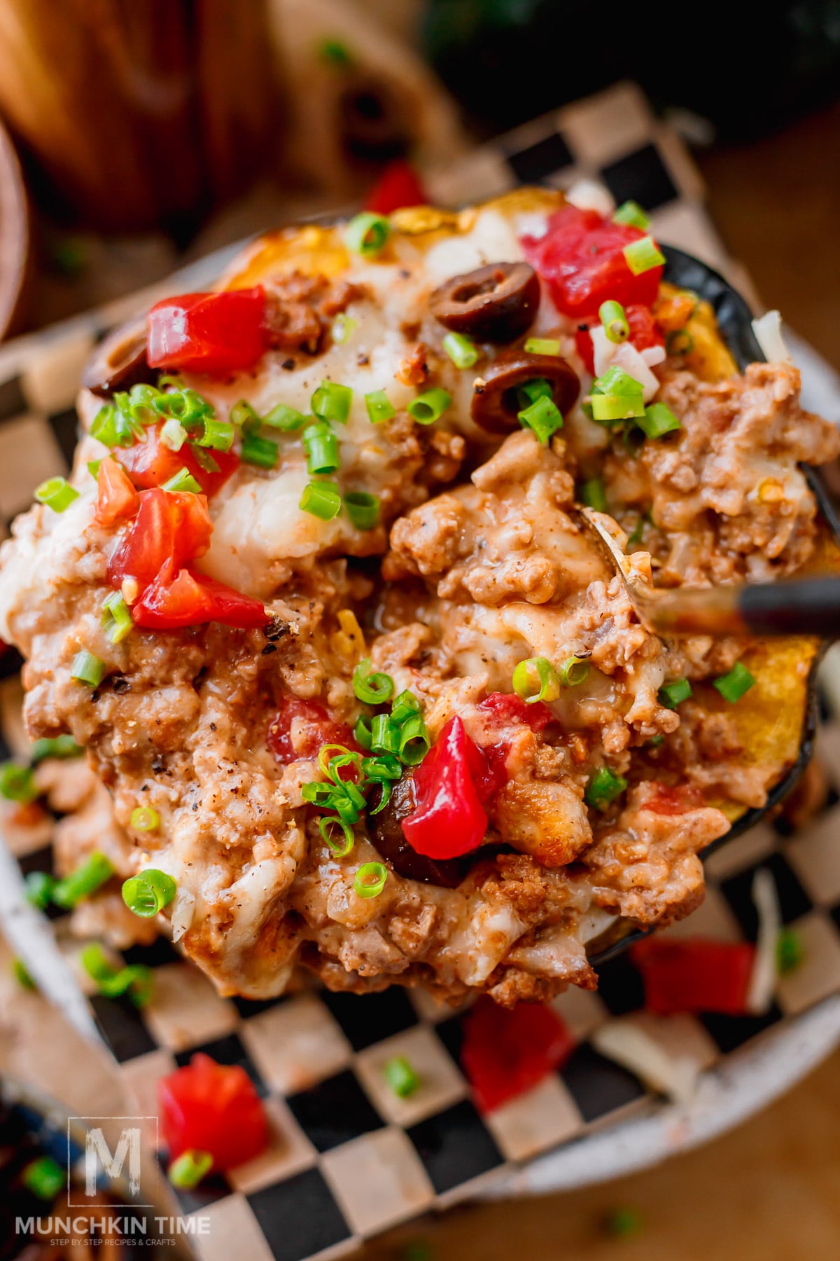 Close-up of cheesy ground beef stuffed acorn squash with melted cheddar and mozzarella, refried beans, fresh tomatoes, avocado, and cilantro.